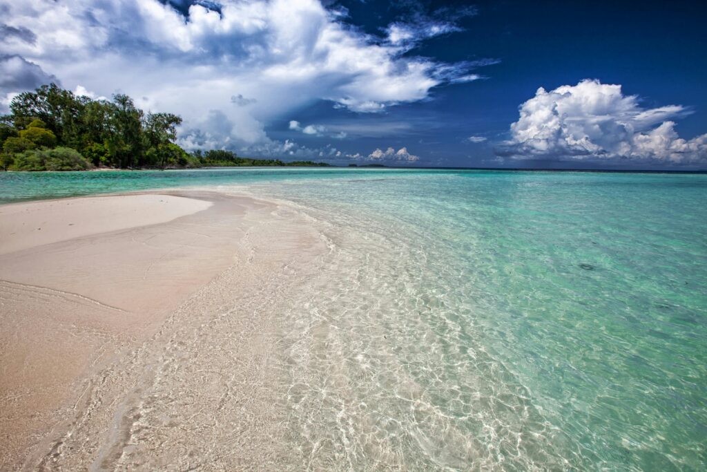 Idyllic tropical beach with clear turquoise water and lush greenery under a vibrant sky.