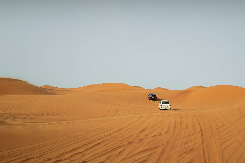 SUVs tread the stunning golden dunes of Dubai under a clear sky, capturing the essence of adventure.